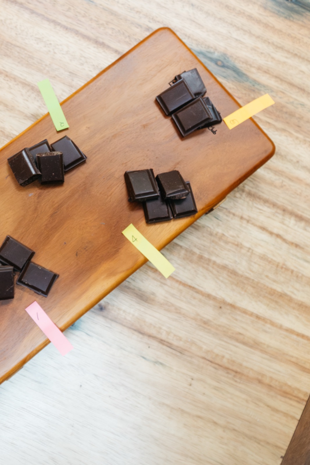 A blind tasting on a wooden board: piles of chocolate squares marked with hidden numbered labels