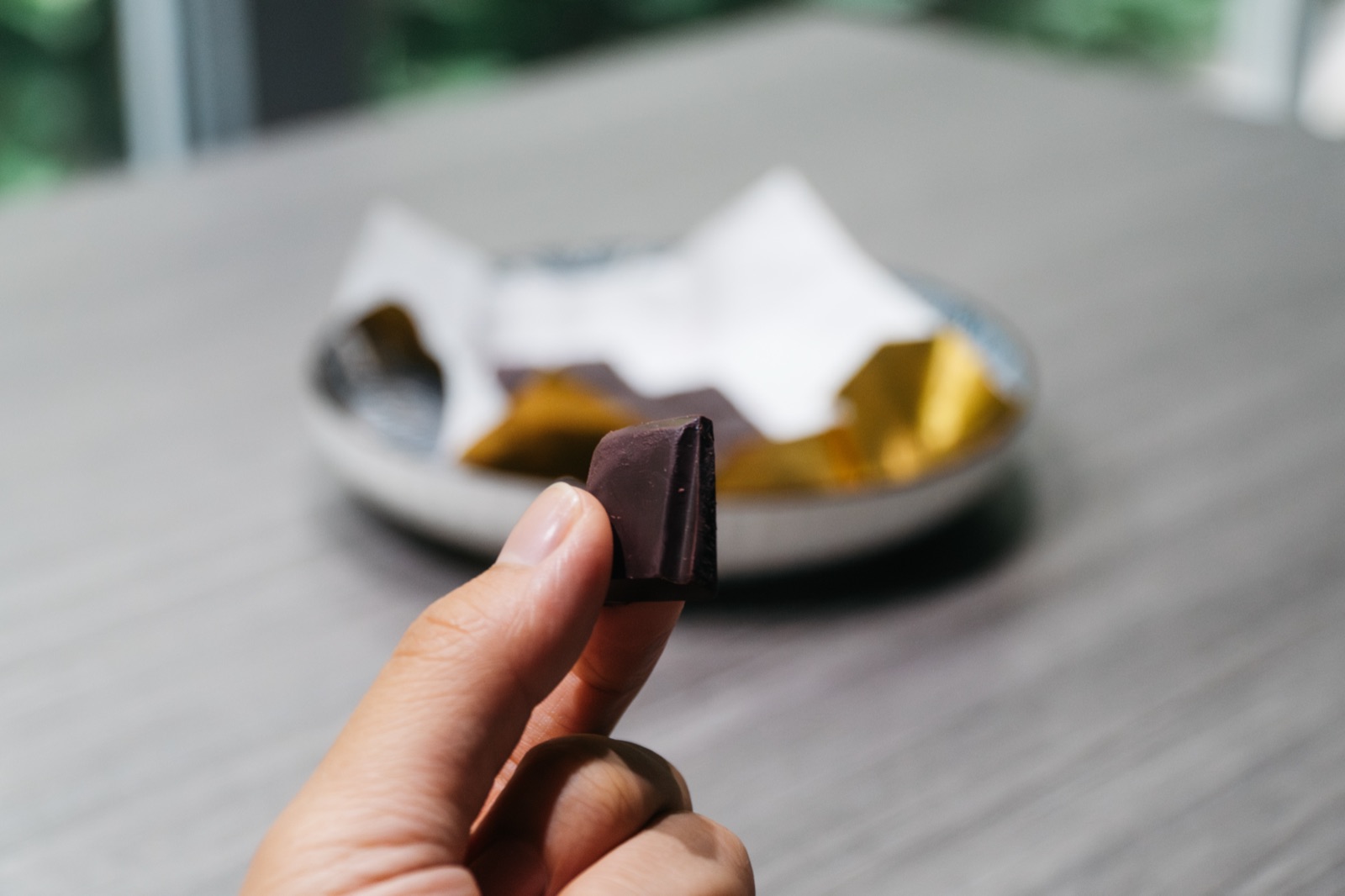 A single piece of the bar held between two fingers, the wrapped bar on a plate behind