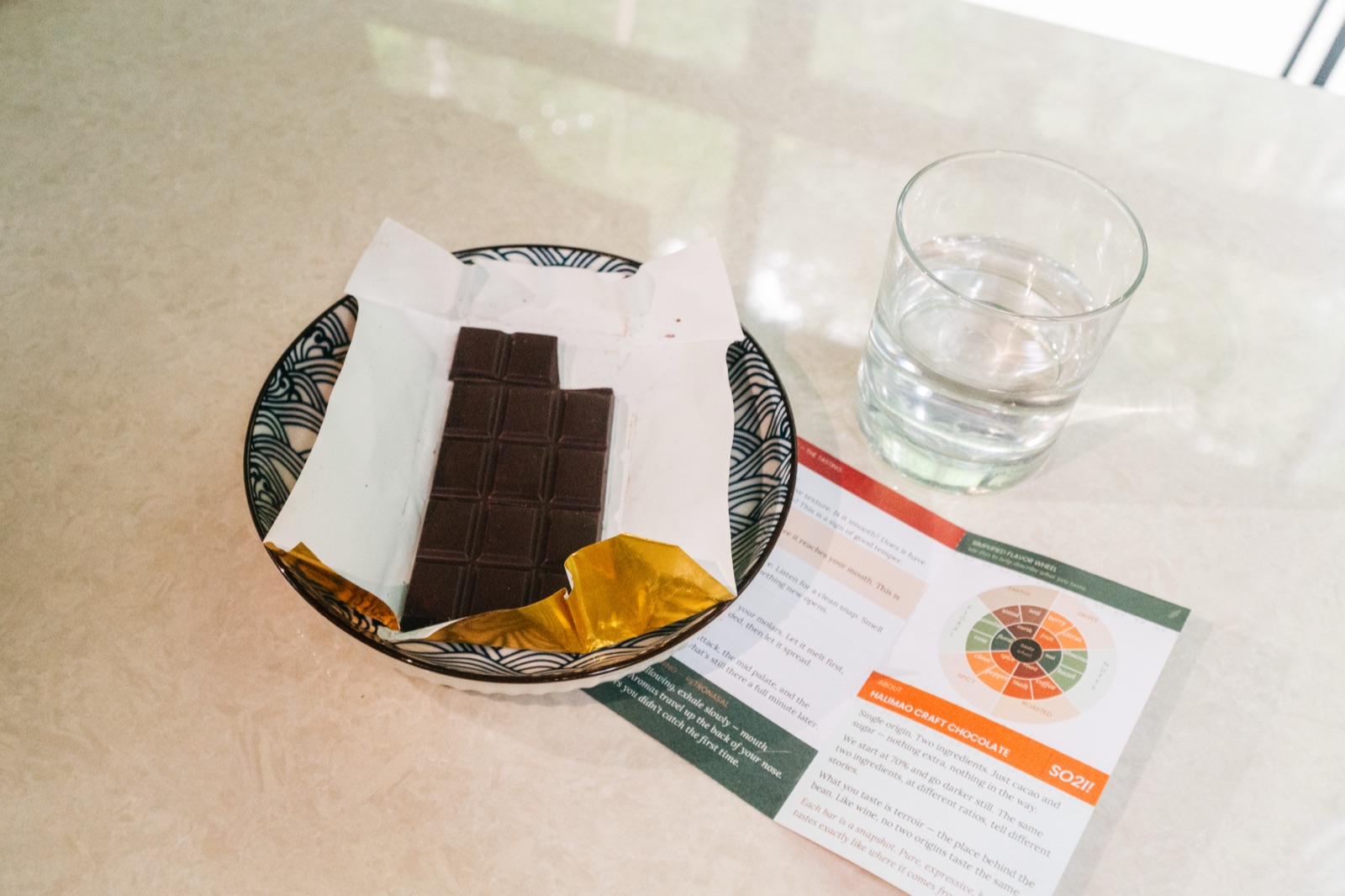 A tasting setup from above: the bar on a patterned plate, a glass of water, and the tasting card